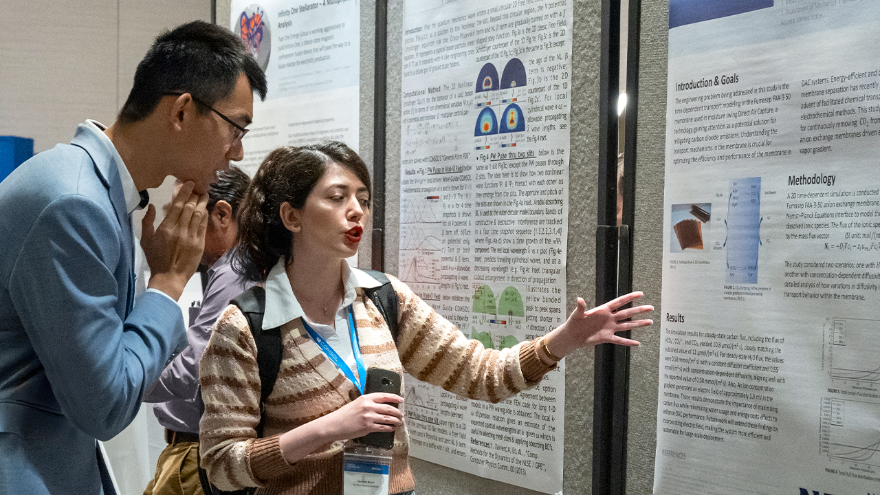 Two COMSOL Conference attendees in the exhibition hall, where one is presenting their work.
